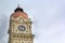 Clock on an urban stone tower against a gray sky with clouds.