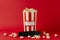 Cloeup of stripped box full of pop corn and black tv remote control on the red background