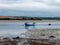 Clonakilty Bay at low tide. A small blue fishing boat is anchored. Open seabed, silt and algae. Picturesque seaside landscape