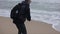 Close back view of a man picking up a stone on the beach and throwing it into the sea