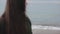 A close blurred side view of a longhaired girl in a dark green coat at the seaside. The focus on the calm sea. Focus