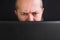 Close of caucasian adult man sitting behind the laptop and typing, black background