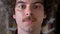 Close footage of student face smiling at camera, bookshelves in background, man with curly man and mustache