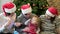 Close friends sitting on the carpet with a baby girll, playing with her and garland near the Christmas tree, dressed in