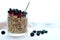 Close glass of granola oatmeal with chia, cranberry and american blueberries on table