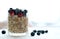 Close glass of granola oatmeal with chia, cranberry and american blueberries on table