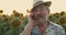 Close happy senior farmer speaking on phone in sunflower field at sunset