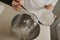 A close photo of the falling wheat flour from the spoon into the steel bowl