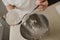 A close photo of the falling wheat flour from the spoon into the steel bowl