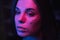 Close portrait of beautiful woman with trendy makeup in violet night light, looking away. Night photo of a brunette in neon light