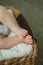 Close portrait of a cute baby 2 months old girl in white clothes in a wicker basket.Little baby feet