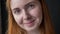 Close portrait of ginger young woman face smiling at camera, cheerful and happy, isolated on black studio background