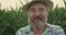 Close portrait of happy senior farmer rejoices at camera in corn field