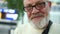 Close portrait of a mature man with glasses and a gray beard. Pensioner smiling sincerely at the airport, shopping