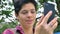 Close portrait of young charming woman having video chat and smiling, standing in park daytime