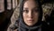 Close portrait of young muslim woman in hijab looking at camera, armed soldier with gun standing behind woman, military