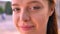 Close portrait of young shy ginger woman looking at camera, street in background, beautiful female smiling outdoors