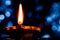 Close shot of a glowing earthen Diya -terracotta lamp, from a low angle with erect flame and a blue background in ambient light