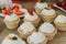 Close shot of many sweet cupcakes on the foreground while a baker decorating the last one.