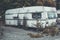 Close shot of an old trailer near plants with tress in the background