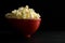 Close Side View of Buttered Popcorn in a Red Bowl Isolated on Black