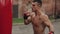 Close side view of muscular male boxer practicing punches and kicks with a punching bag being outdoors