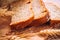 Close slice of fresh bread with poppy seeds and wheat ears on wooden background