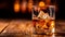 Close to the camera, a glass of whiskey with ice on a wooden table on a black background.