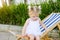 Close up Adorable blondy baby girl in dress or toddler child sitting and relaxing on a sunbed or a deckchair in the city park recr