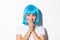 Close-up of adorable dreamy asian girl looking left and smiling, clasping hands together hopeful, wearing blue wig for