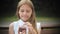 Close up of adorable little girl eating a cake with her hands sitting on a bench in the park