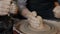 Close-up of adult and child`s dirty hands molding clay into ceramic pot on throwing wheel