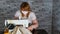 Close up of adult woman stitching curtain, using sewing machine. Young seamstress in medical mask working on sewing