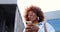 Close up of African American joyful young stylish woman tapping or scrolling on smartphone and standing at city street