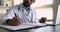 Close up African general practitioner use laptop writing in casebook