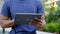 Close up afro-american man courier food delivery sitting on bench uses tablet