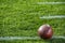 A close-up of an American football sitting on a white yard line with hash marks.