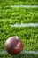 A close-up of an American football sitting on a white yard line with hash marks.