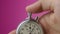 Close-up analog stopwatch in man`s hand on pink background is starting and stopping