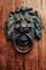 Close up of antique metal doorknob with lion head on brown wooden door. Old bronze traditional knocker.