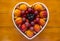 Close-up of appetizing plate of seasonal ripe fresh fruit in a white heart-shaped plate - healthy eating with apricots, grapes,