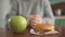 Close up apple and burger lying in front of blurred figure of unrecognizable chubby girl. Hand of woman wants to take