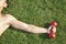 Close up on arm and shoulder holding red dumbbell in grass, view from above