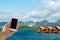 Close up of Asian Male Hand Holding Smart Mobile Phone with Blank Screen on Sea, Blue Sky and Luxury Floating Hotel while Travel