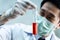 Close-up of Asian male scientist in white uniform holding laboratory flask with red chemical solution. Chemistry