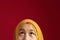 Close up of Asian muslim teenage girl wearing yellow hijab looking up and thinking, half face portrait with copy space above, red