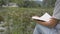 Close up asian woman in casual dress is sitting on the grass near natural pond with lotus and reading a novel happily.