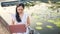 Close up Asian woman in a white dress sitting next to a lotus pond, working with laptop in a public park