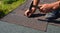 A close-up of asphalt shingles installation on the roof edge. A roofer is nailing asphalt shingles to the roof deck covered with