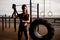 Close-up athletic woman with sledgehammer stands near big tire